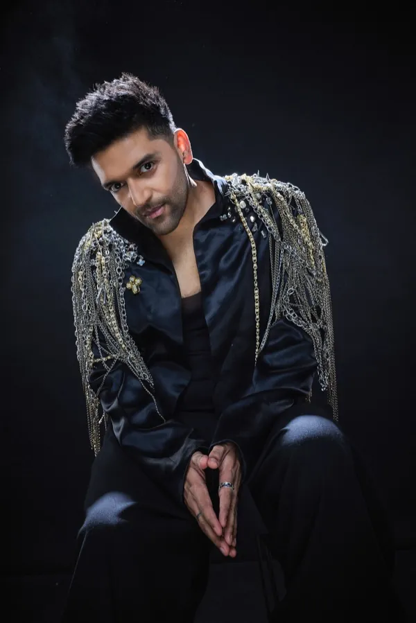 Guru Randhawa seated, in a black jacket with chain fringe