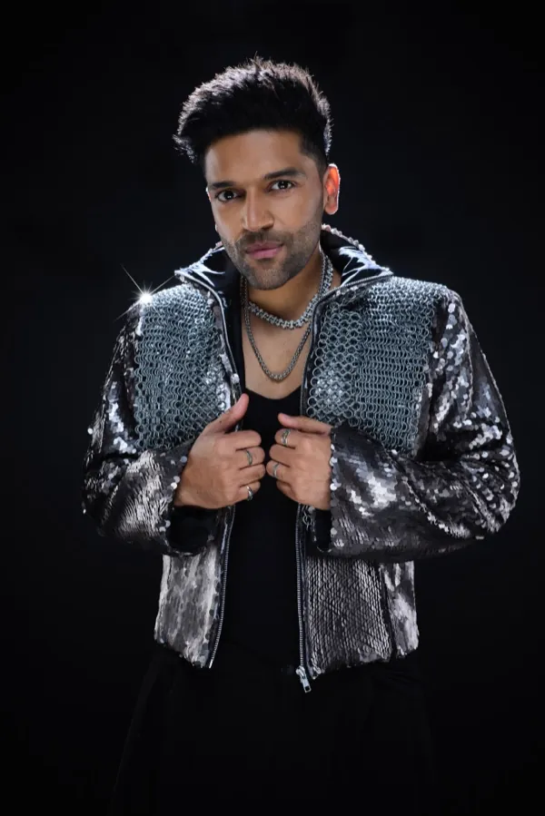 Guru Randhawa holding his jacket open, chains at his neck