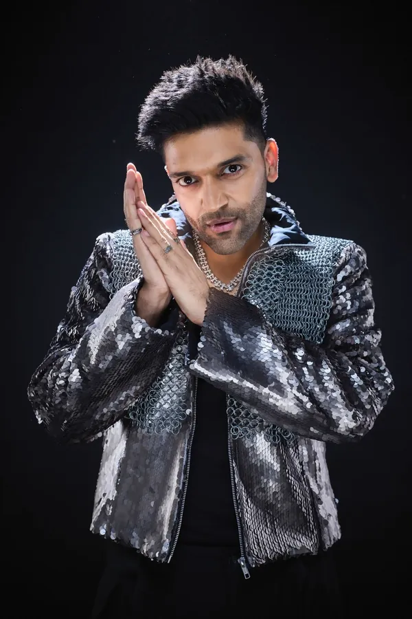Guru Randhawa with his hands pressed together, in a silver sequin jacket