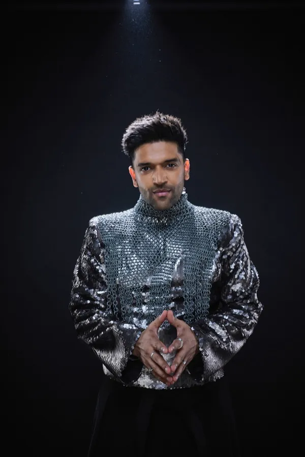 Guru Randhawa under a spotlight, fingers steepled