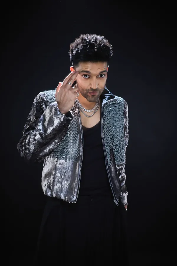 Guru Randhawa smiling, two fingers at his temple